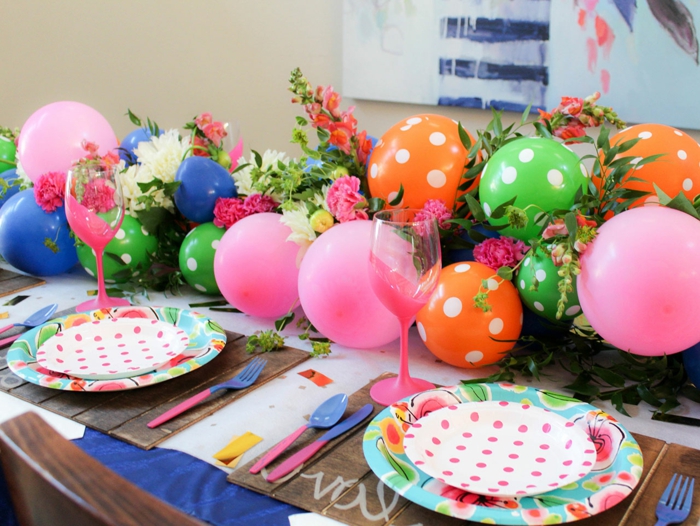 ballons aux couleurs différentes groupées en arche décorative, verres roses, assiettes et ballons pointillés, roses et feuillages