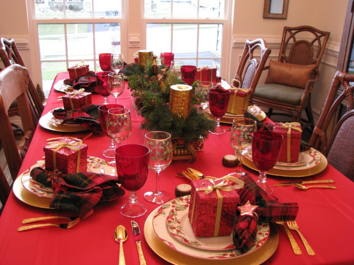 nappe de table rouge, cadeaux enveloppés en papier lumineux rouge, branches de pins, serviettes aux couleurs de noel, chaises vintage, assiettes aux motifs floraux