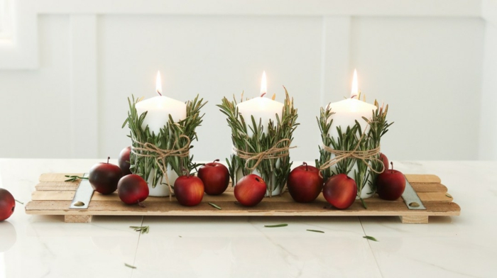 déco de table pour Noël planche de bois, pommes rouges, bougies blanches enveloppées de brins de romarin