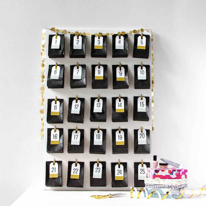 calendrier de l avent beauté original en sachets noirs avec des étiquettes cadeau aux chiffres collées sur un panneau blanc accroché à un mur