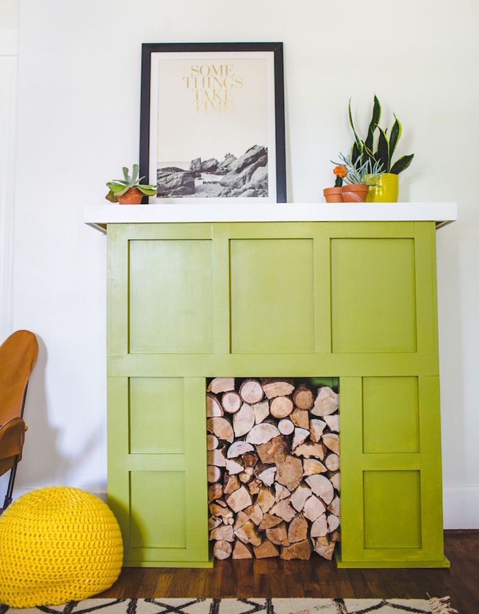 faux manteau cheminée décorative vert pomme sur mur blanc avec stock buches dans insert sur parquet bois ciré et petits pots de cactus