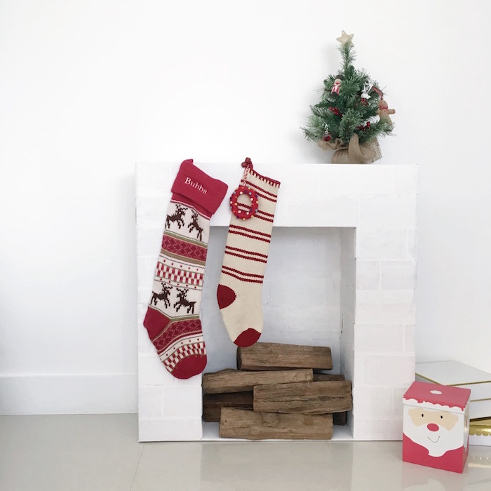 modele petite fausse cheminée de déco imitations briques blanches sur mur blanc avec buches en bois et déco de noel avec chaussettes mini sapin