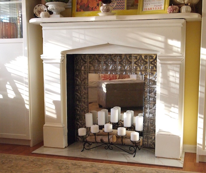 cheminée déco avec manteau blanc et fond insert en métal forgé et chandelier bougies blanches et mini buches décoratives 