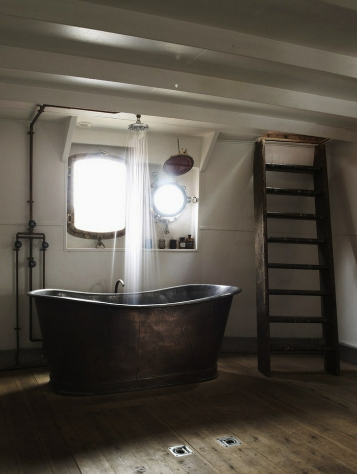 salle de bain simple, grande baignoire en fonte, échelle en bois, plafond blanc, sol en bois, douche apparente, miroir et éclairage avec lampe industrielle