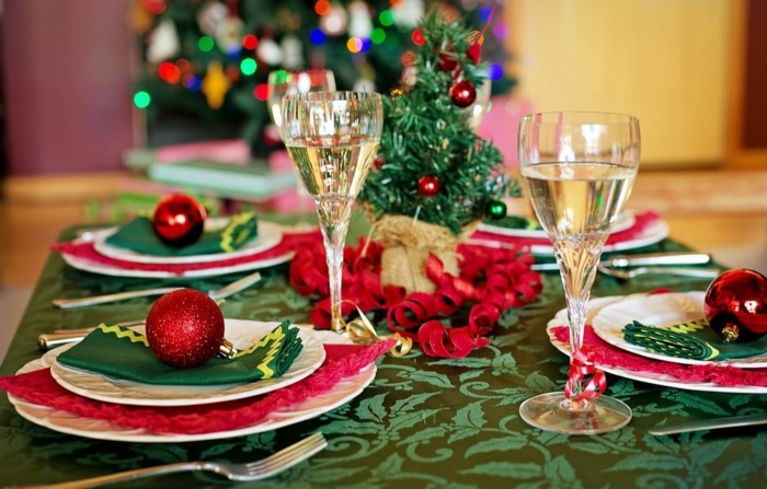nappe de table verte aux motifs floraux, petit sapin décoratif, boules décoratives rouges, serviettes vertes, verres à champagne