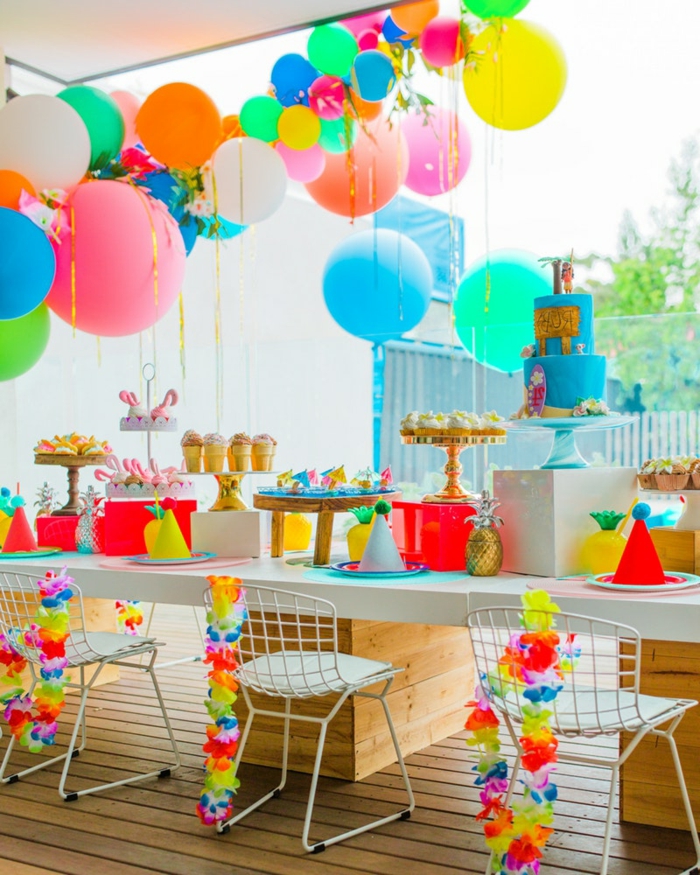 chaises blanches, table blanche, ballons suspendus, présentoir à gâteau avec gâteau bleu et plateaux dorés avec cupcakes