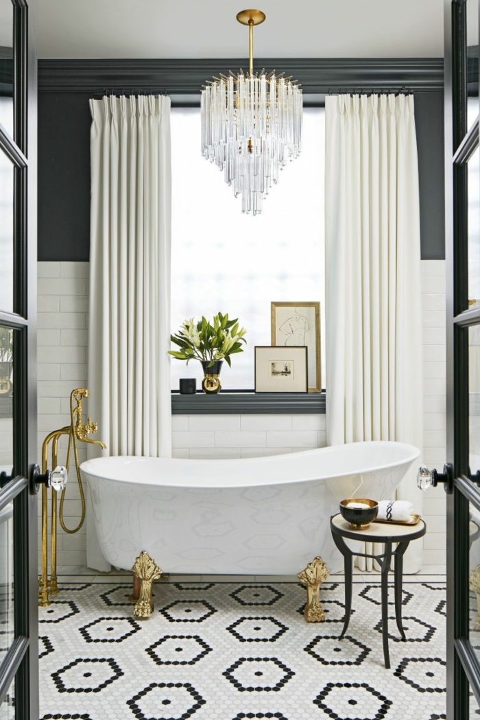 salle de bain en noir et blanc, grand plafonnier en cristal, tabouret tripode, robinet doré, rideaux lourds blancs, éléments de métal doré