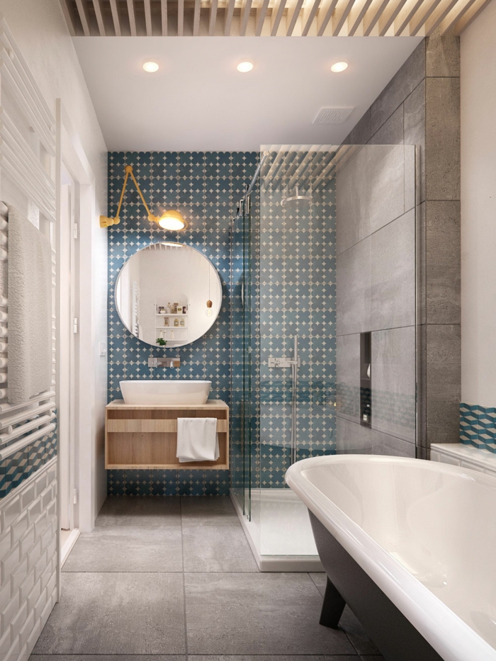 salle de bain en bleu et blanc, miroir rond, lampe murale jaune, meuble sous vasque bois, carrelage en vert et blanc et carreaux imitation béton