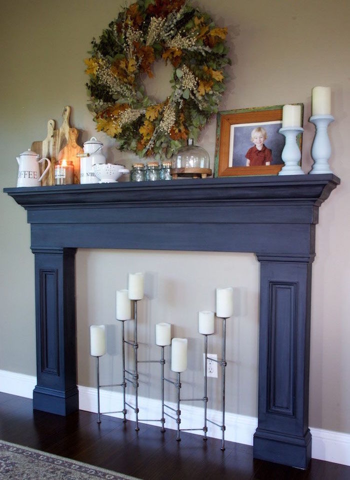 meuble en bois manteau de cheminée noir en bois avec support bougies design contre mur fris taupe et couronne végétale murale 