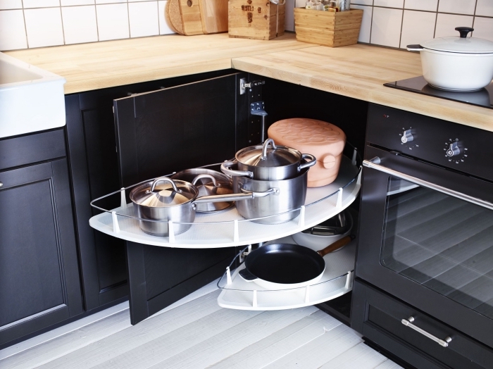 un meuble d'angle cuisine bas avec deux plateaux en mélaminé qui sortent pour accéder facilement à la vaisselle de cuisine, des placards de cuisine bas en bois et noir, contrastant avec les murs et le sol blancs
