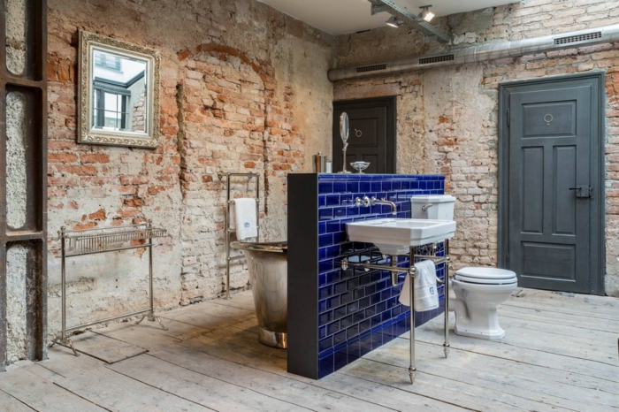 salle de bain au design brut, murs en briques, cloison bleue aux carreaux luisants, porte-serviette industriel, éclairage industriel