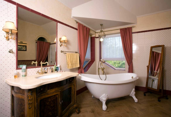 miroir sur pieds en bois, baignoire blanche, lavabo bois et blanc, rideaux rouges, papier peint blanc, sol parquet