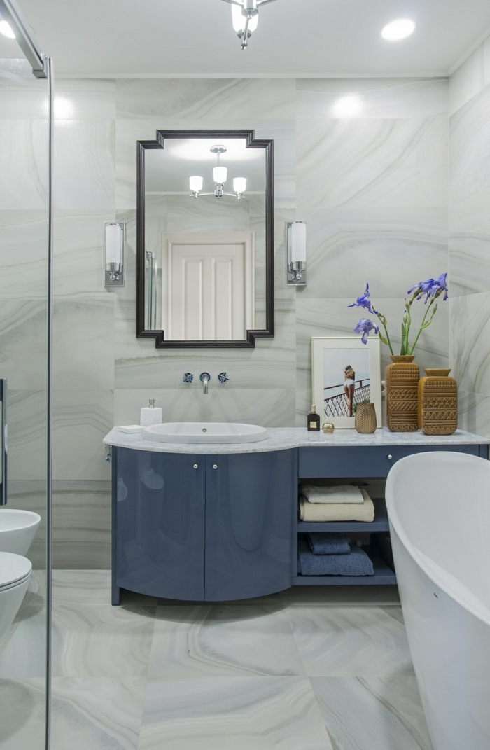 baignoire ovale vintage, sol marbré, vases marron avec fleurs bleues, grand miroir encadré, meuble sous lavabo bleu 