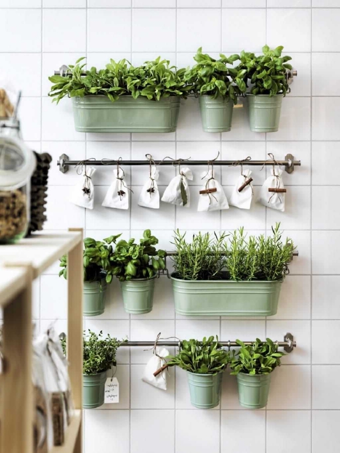 créer un petite jardin d'herbes aromatiques dans la cuisine à l'aide de jardinières en zinc couleur vert amande et des pochettes en toile suspendues sur des barres de support murales, sur le fond du mur revêtu de carrelage bmanc