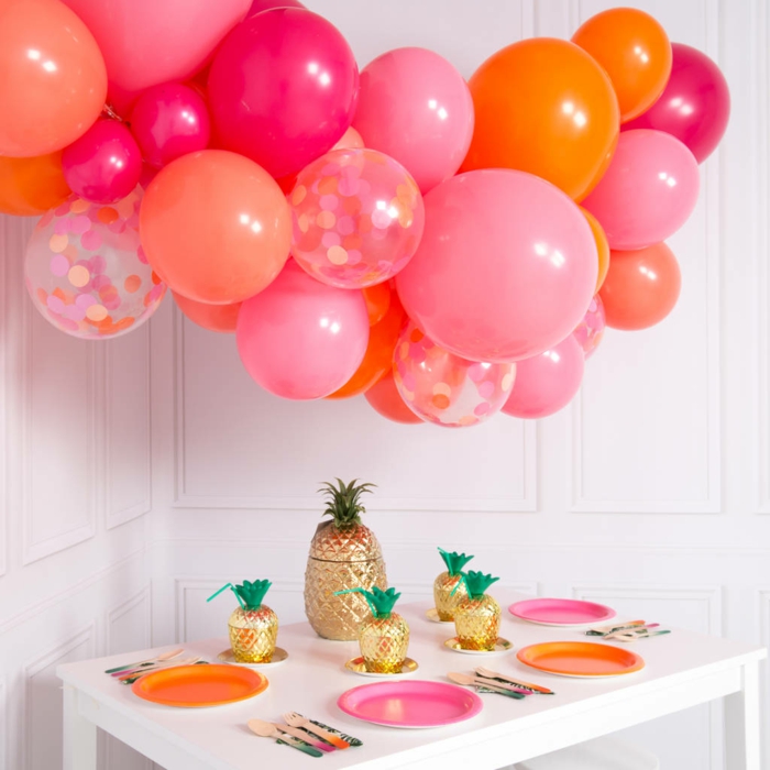 nuage de ballons en rose et orange, ananas dorés, assiettes aux couleurs des ballons, petite table blanche