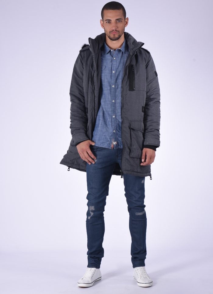 look homme urbain chic avec un modèle de parka technique chaud couleur gris avec grandes poches et capuche amovible, porté de façon casual chic avec un jean slim et une chemise imitation denim