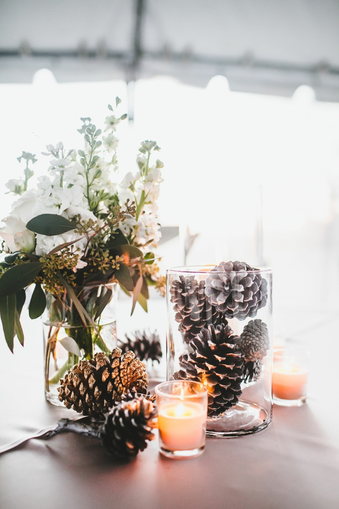 bocaux en verre, pommes de pin, petite bougie allumée, bouquet champêtre, décoration magique pour les fêtes d'hiver