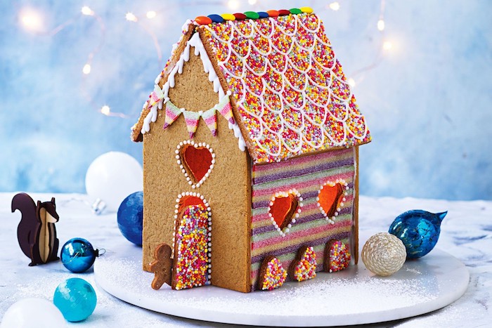 maisonnette gourmande de noel au gingembre avec toiture décorée de vermicelles colorées, mur à rayures colorés et porte vermicelles