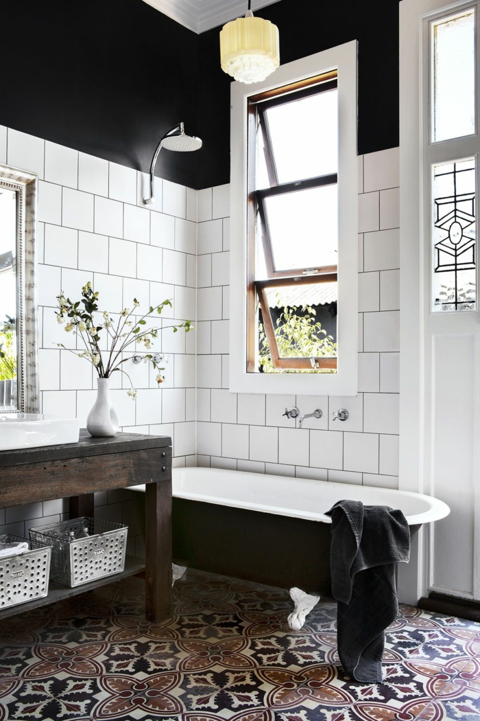 déco de salle de bain en noir et blanc, baignoire en fonte noire et blanche, carreaux blancs et sol carreaux de ciment; murs noirs