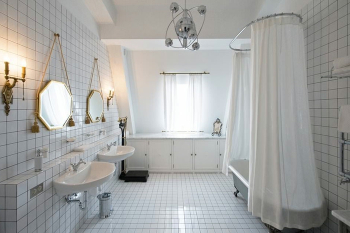 salle de bain toute blanche, miroirs octogonaux au cadre doré, carreaux blancs, lavabo rétro blanc, baignoire ancienne