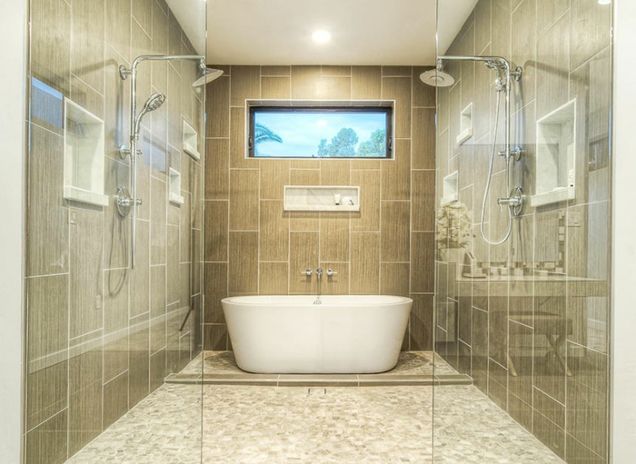 baignoire blanche, sol beige en petites tuiles, deux douches à l'italienne, espace pratique et commode
