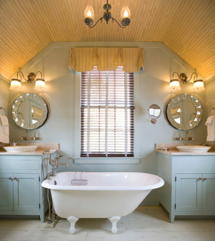 baignoire asymétrique, miroirs ronds art déco, deux lavabos et meubles sous lavabo bleus, plafond en pente