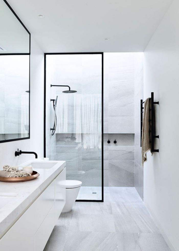 salle de bain au design sobre, tête de douche ronde, vasque blanche minimaliste, plateau cuivré rond, cloison verrière profilé noir