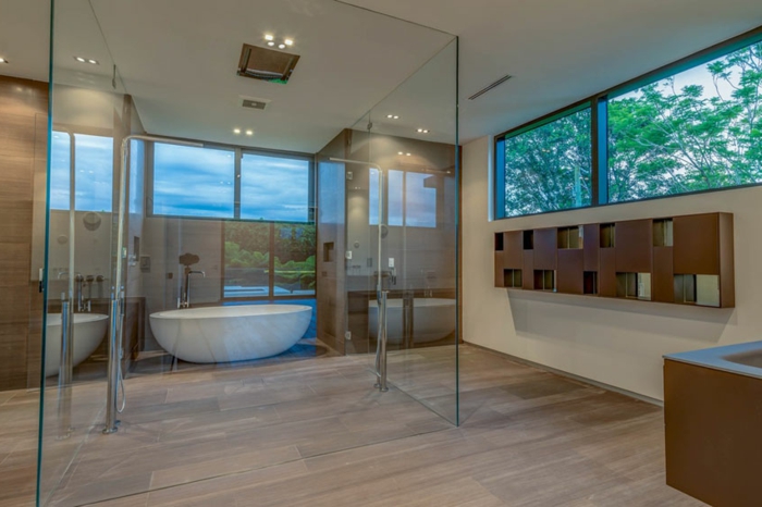 salle de bain élégante, carreaux travertin, grandes fenêtres panoramiques, baignoire blanche ovale, cloisons en verre