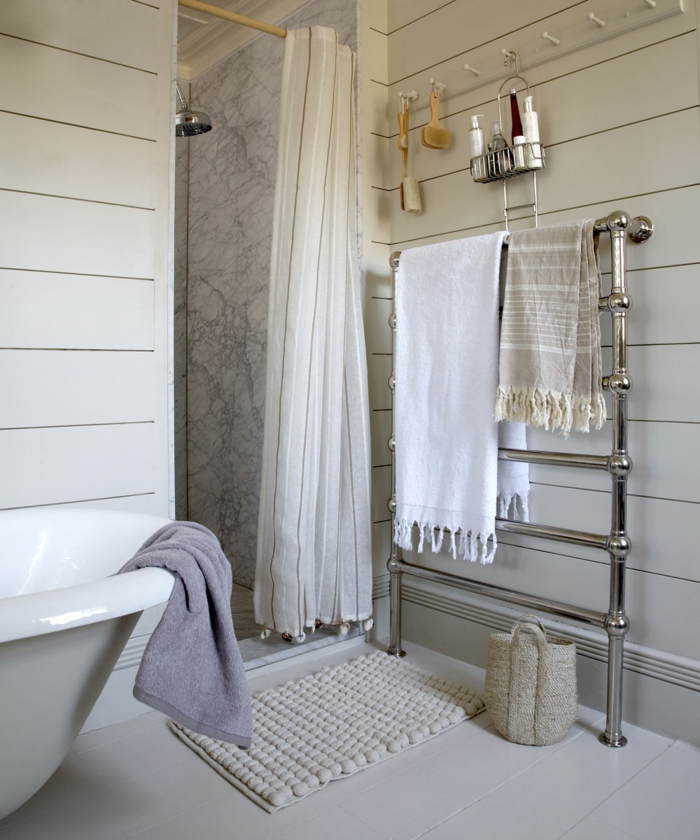 baignoire îlot et douche avec cloison blanche, rideau blanc, porte serviette chromé, tapis antidérapant et panier en fibres naturels