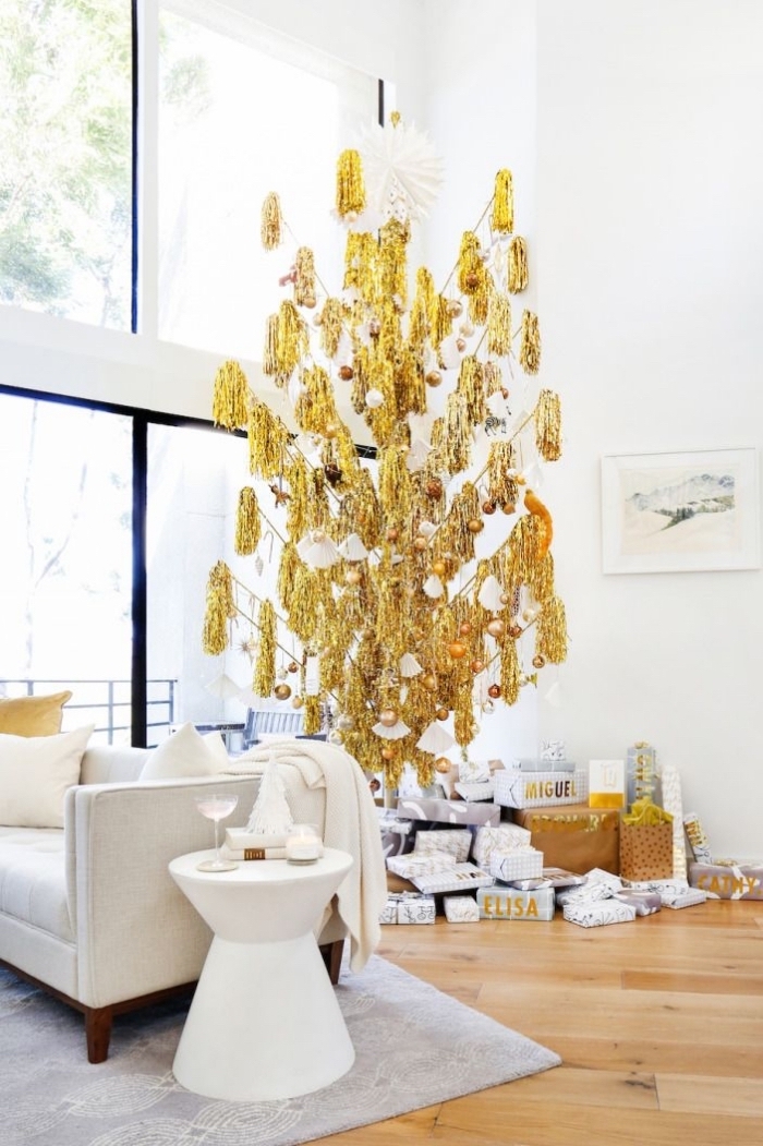 sapin de noe artificiel de luxe à franges dorées, posé à l'envers et suspendu au plafond dans un salon moderne en bla