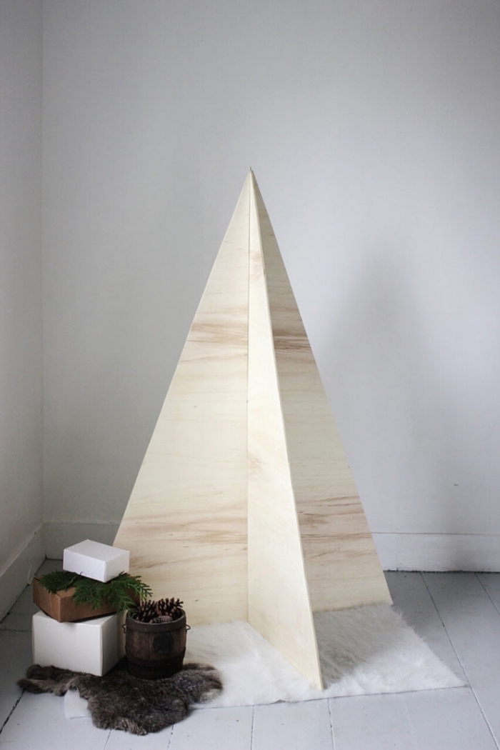 sapin de noel en bois au design minimaliste, fait avec des planches en bois clair, pour une déco de fête de style scandinave, sapin décoratif en bois posé sur un tapis cocooning blanc