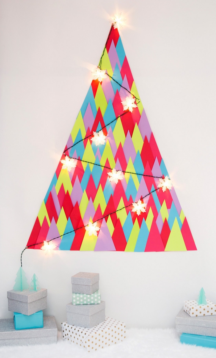 sapin de noel mural réalisé à partir de triangles en papier de couleurs différentes, orné d'une jolie guirlande lumineuse, decoration de noël à fabriquer en papier pour une petite chambre 