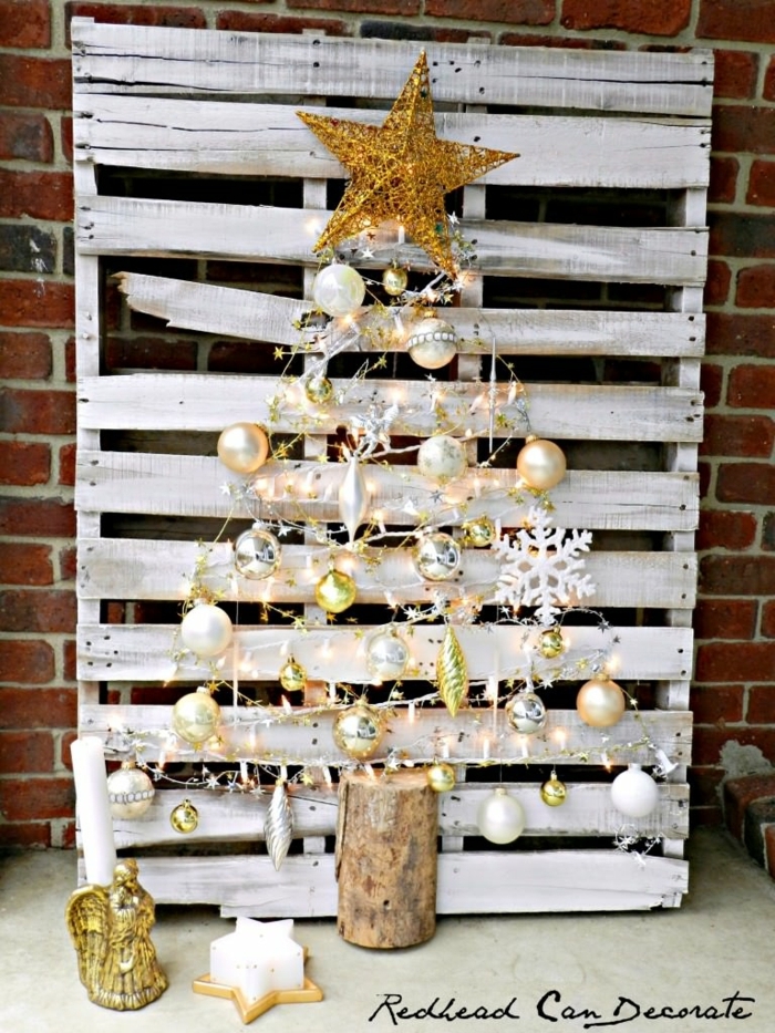 palette blanche avec décoration féerique, tronc de bois, grande étoile jaune, boules dorées et argentées, mur en briques