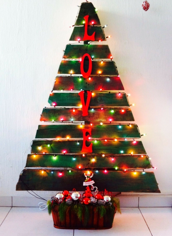 arbre de noel chaleureux aux ampoules colorées, jouets de noel empilés et verdure, grandes lettres décoratives, sapin en palettes