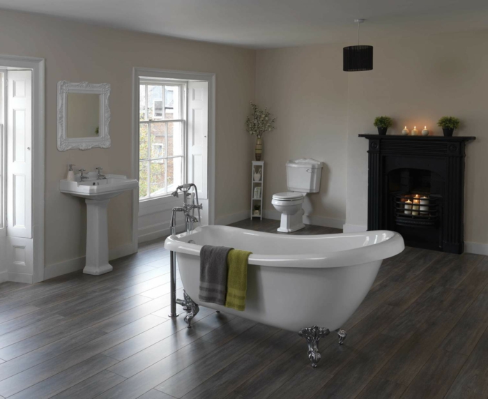 salle de bain spacieuse avec le sol en bois, baignoire centrale asymétrique, lavabo colonne, cheminée avec bougies 