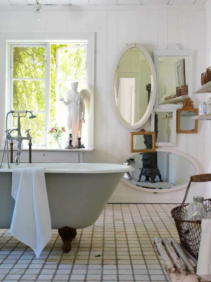 salle de bain antique, miroir ovale blanc, grande baignoire centrale, sol carreaux blancs, poêle rustique, lambris blanc