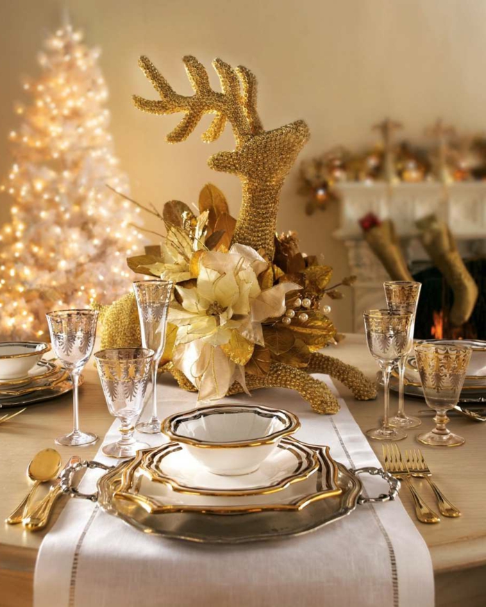 sapin blanc lumineux, table décorée pour les fêtes, service de table élégant, cheminée blanche, statuette cerf, chemin de table blanc