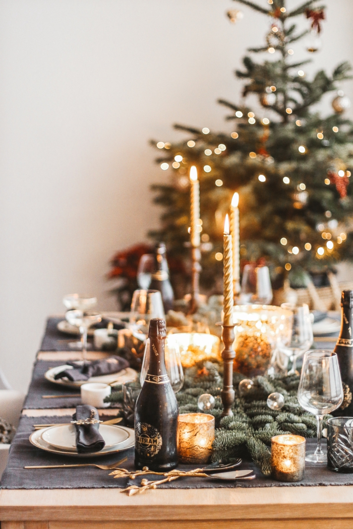 table de repas en bois décorée pour Noel, bougies allumées, grand arbre de noel, branches de pin artificielles