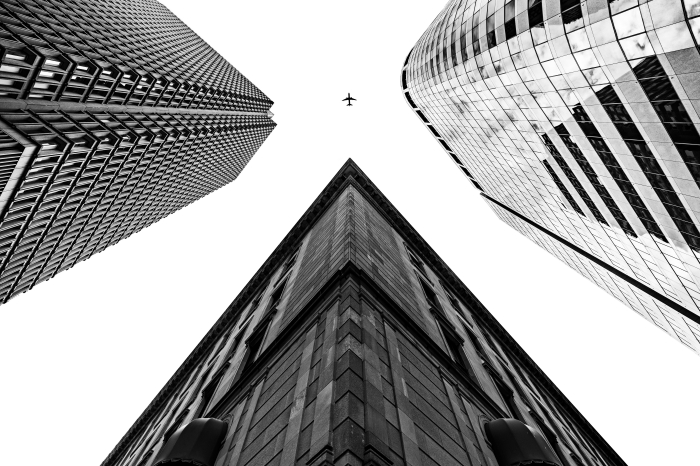 belle photo noir et blanc d'un avion dans le ciel entre trois grands bâtiments, paysage urbain avec perspective originale