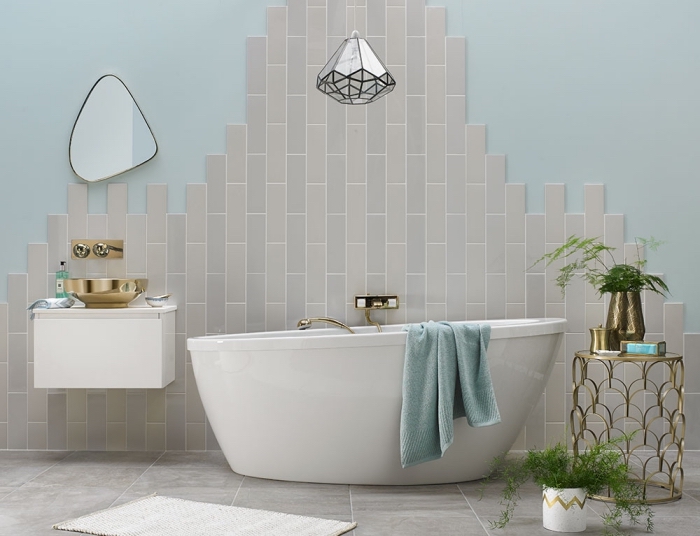 carrelage mural posé sur le mur derrière la baignoire d'un aspect inachevé, meuble sous vasque suspendu avec vasque à poser en laiton
