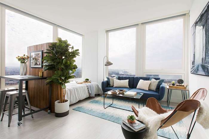 idee amenagement studio 20m2 avec un canapé bleu marine, lit blanc, table basse verre et métal, cloison bois amovible
