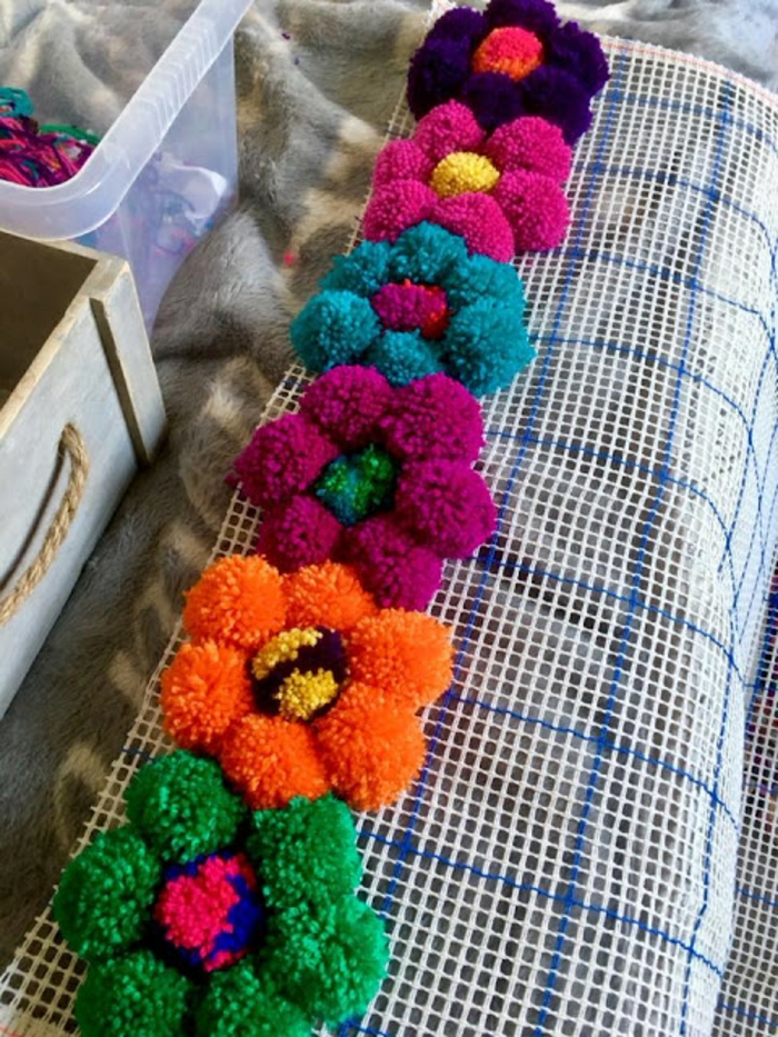 pompons multicolores arrangés en fleurs, diy pompon et diy tapis à réaliser tout seul, toile à canevas pour tapis