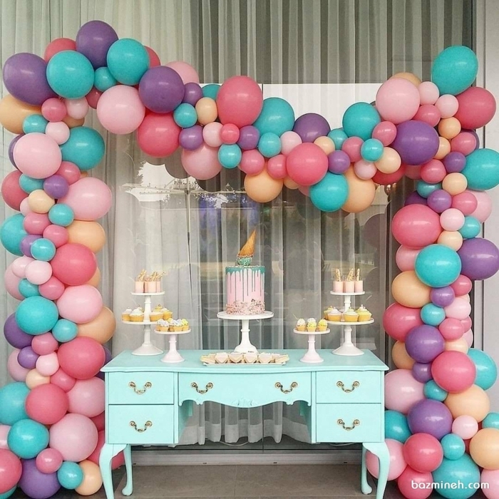 ballons roses et bleus autour d'une commode turquoise, gâteaux cupcakes avec muffins et grand gateau glaçage rose et bleu