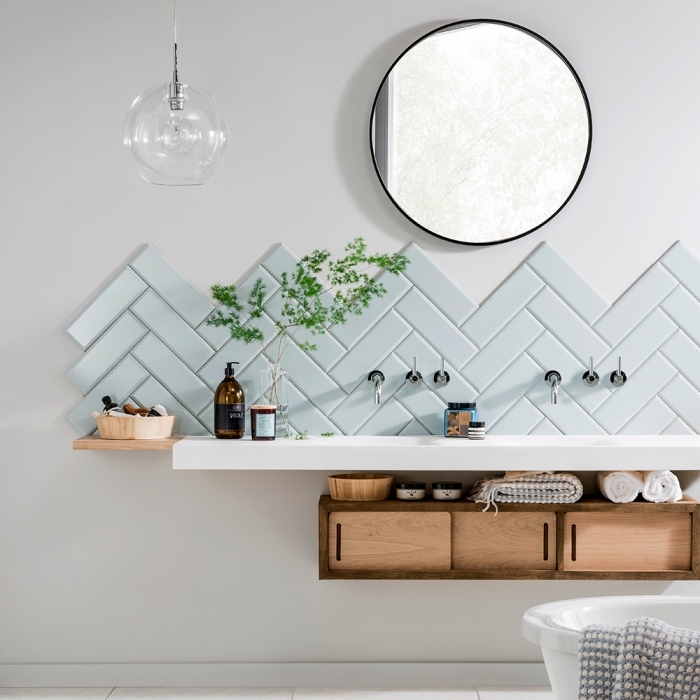 ambiance naturelle et apaisante dans une salle de bains scandinave, crédence salle de bain de carrelage en chevron de couleur vert menthe pâle surmonté d'un miroir rond tendance