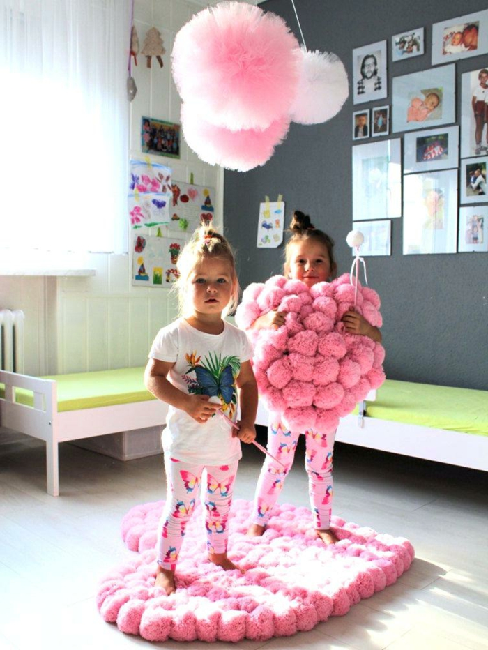 chambre d'enfant décorée de tapis et de coussin pompon en forme de coeur, suspensions rondes en tulle rose et deux petites filles