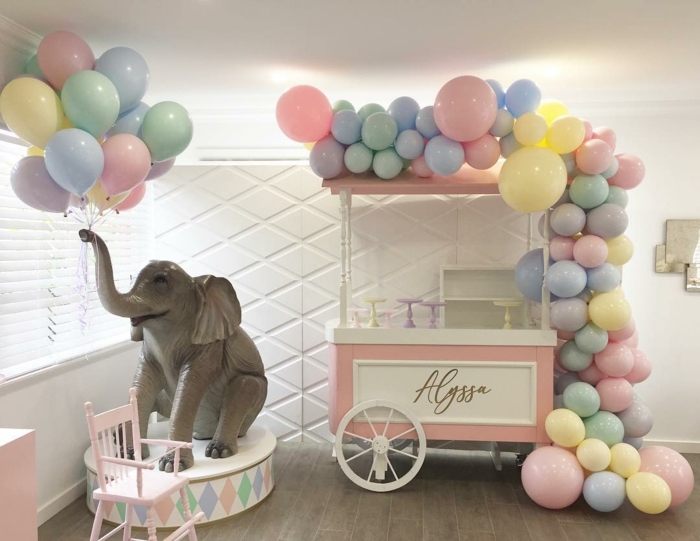jouet éléphant qui porte une brassée de ballons, charrette en rose et blanc décorée d'une arche en ballons de tailles et couleurs diverses