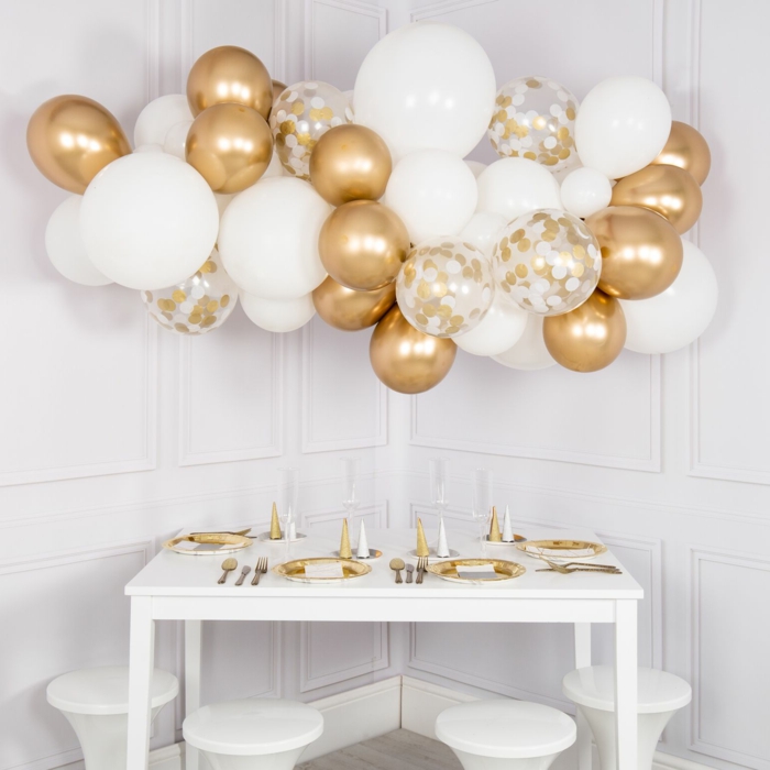 déco de fête nuage de ballons dorés et blancs, table blanche arrangée avec assiettes en blanc et doré, ballons à paillettes