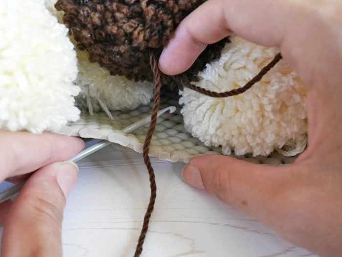 tapis en pompons marron et blancs, aiguille à tricoter, toile canevas pour tapis en pompon