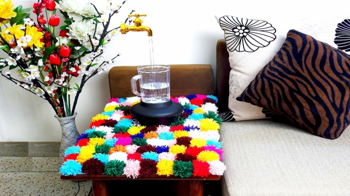 table de chevet décorée d'un tapis pompon multicolore, bouquet de fleurs artificielles, coussins décoratifs motifs animaux