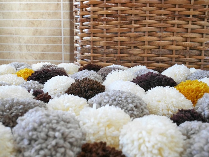 grand panier rustique en fibres tressés et tapis pompons, pompons gris blancs, jaunes, marron assemblés en joli tapis